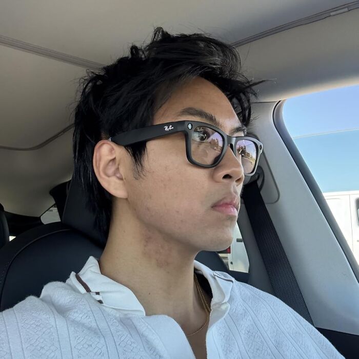 Person wearing black Ray-Ban glasses sitting inside a car with Black Friday deals visible in reflections on lenses.