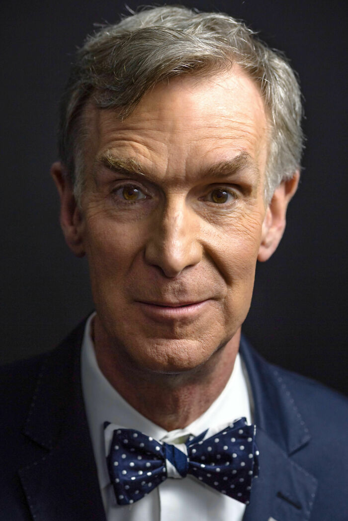 Bill Nye smiling, wearing a navy suit and polka dot bow tie, close-up portrait highlighting his bio and career.
