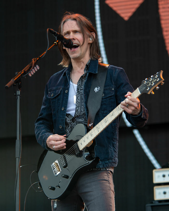 Myles Kennedy singing and playing electric guitar on stage during a live music performance in casual denim jacket.
