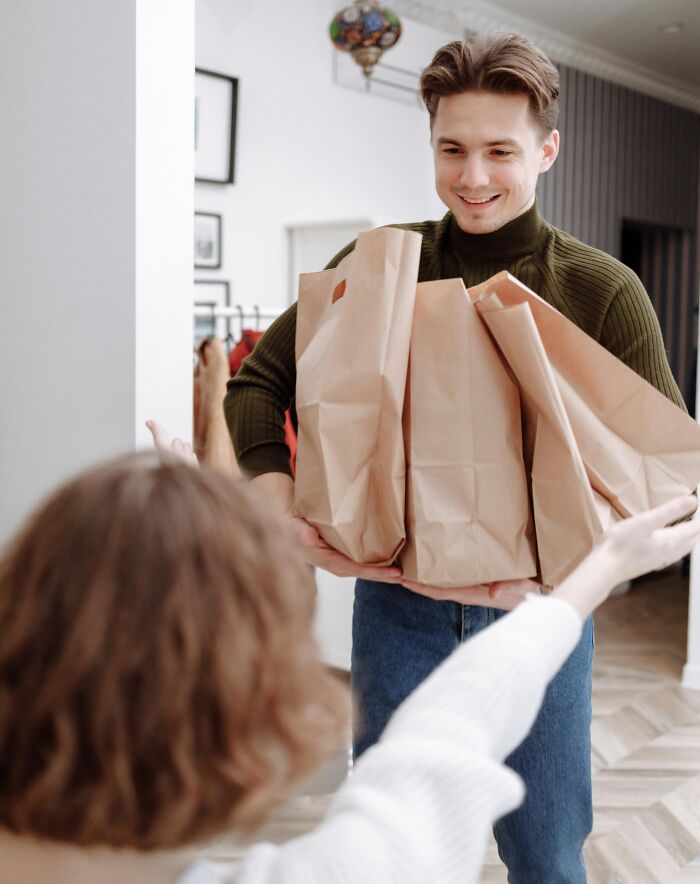 Young man carrying many paper bags while a woman reaches out to help, showing relatable everyday moments and common habits.