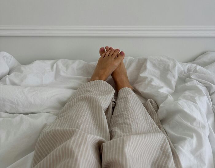 Person in striped pajamas lying on bed with feet up, representing relatable and ridiculous everyday moments.
