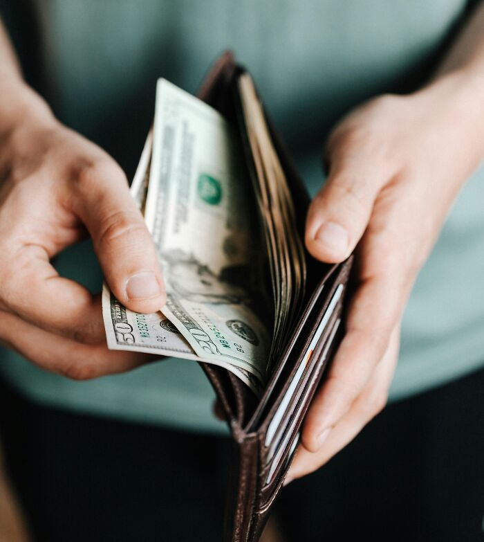 Hands holding a wallet with cash inside, illustrating relatable and ridiculous everyday moments we’re all probably guilty of.