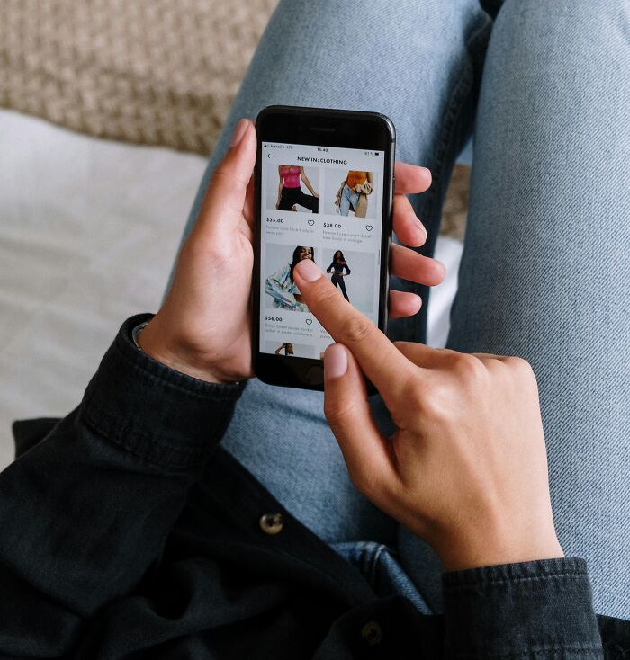 Person scrolling through clothing options on a smartphone, showing a relatable and ridiculous online shopping habit.