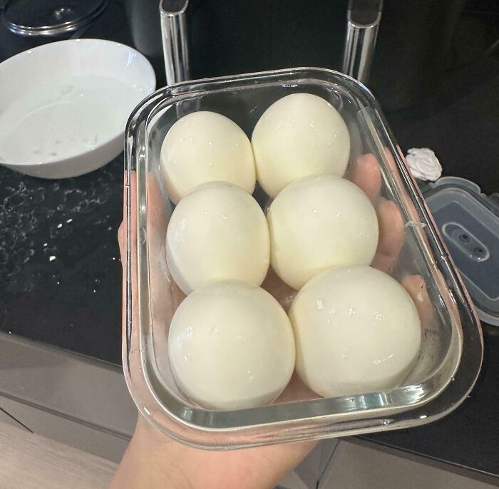 Six peeled hard-boiled eggs perfectly aligned inside a rectangular glass container, showcasing precise food arrangement.