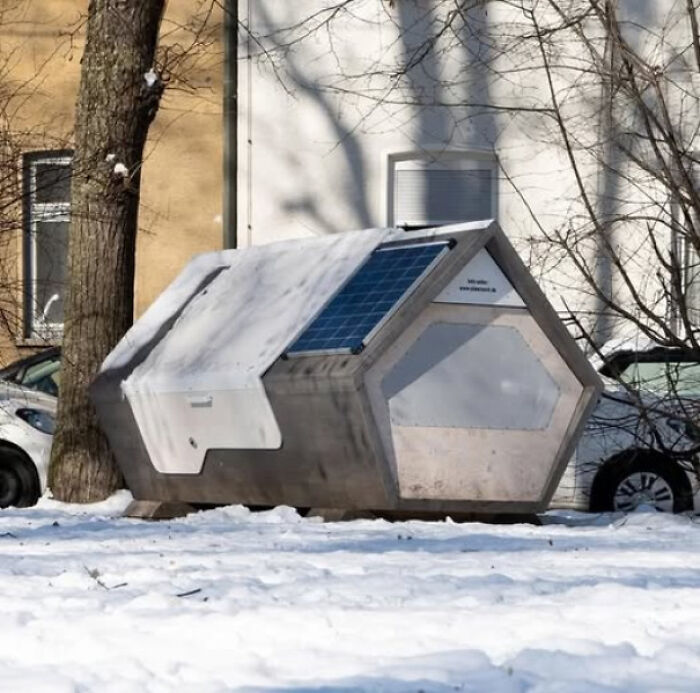 Small hexagonal shelter in snowy urban area with solar panel, exploring themes of existence, reality, and the universe.