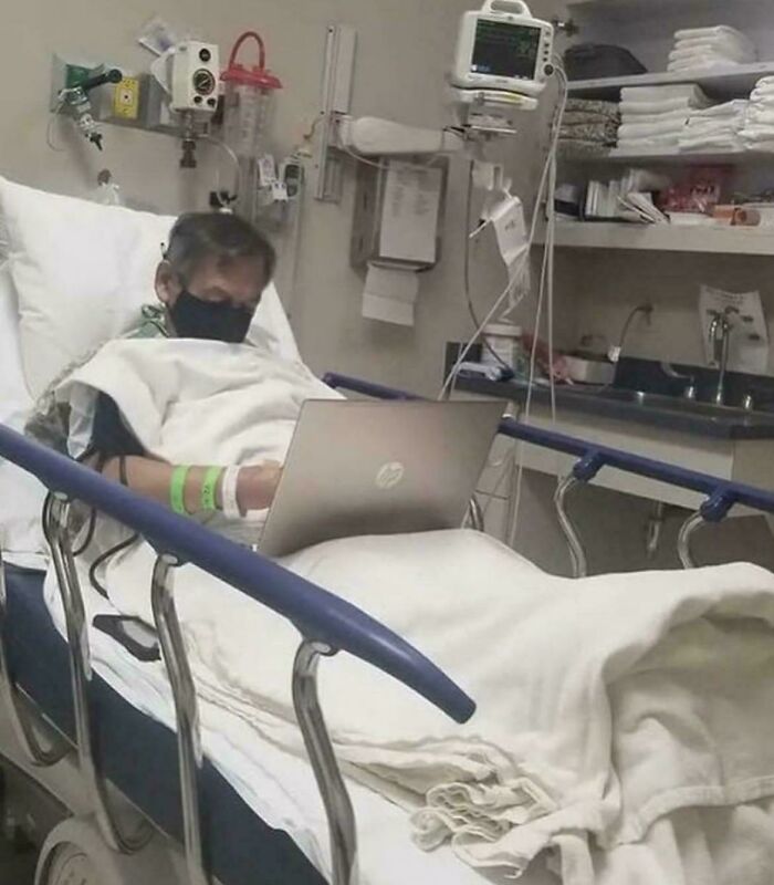 Patient working on laptop in hospital bed surrounded by medical equipment reflecting existence, reality, and the universe concepts.