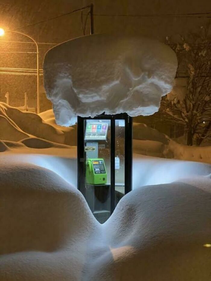 Snow-covered phone booth at night with glowing light, invoking thoughts on existence, reality, and the universe.