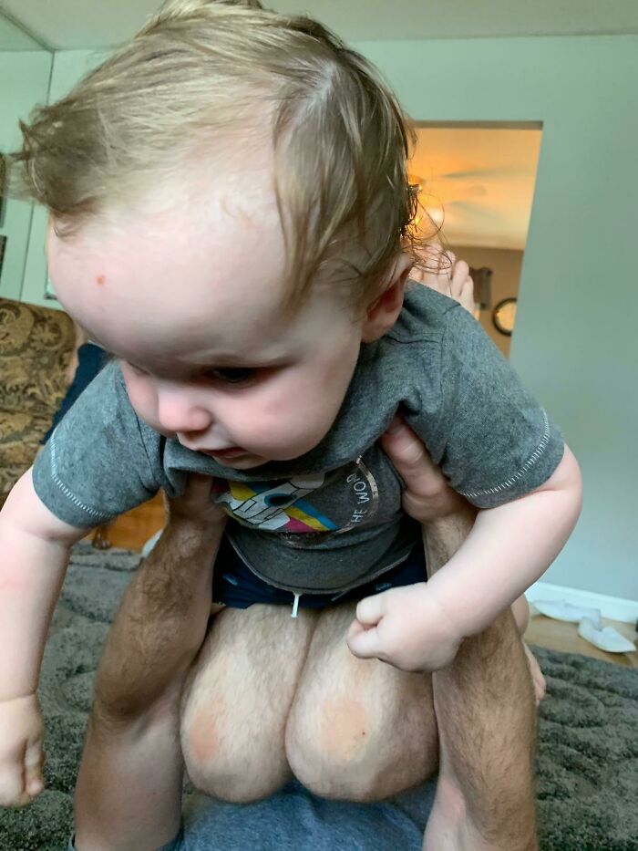 Baby held above an adult whose knees look like a head, one of the confusing photos that tricks your brain.