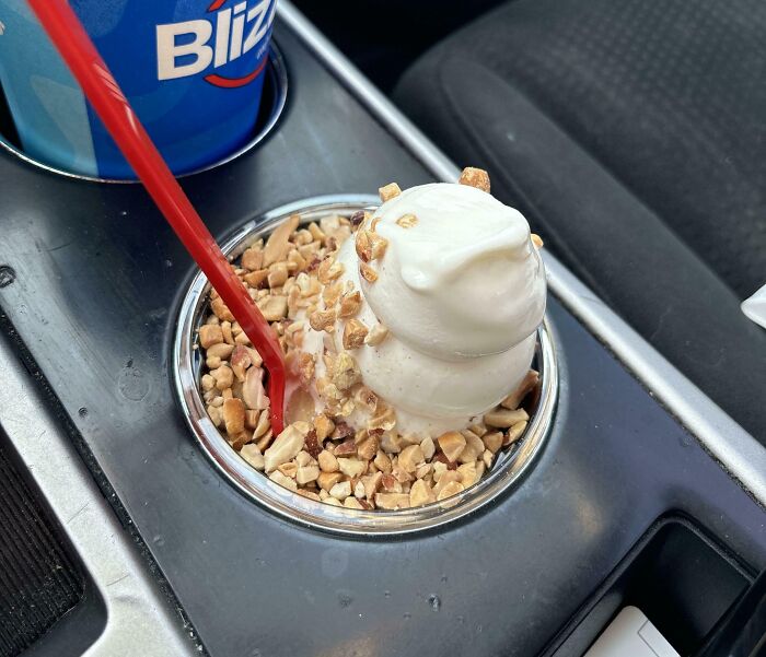 Soft serve ice cream perfectly fits car cup holder filled with crushed nuts and a red spoon inside.