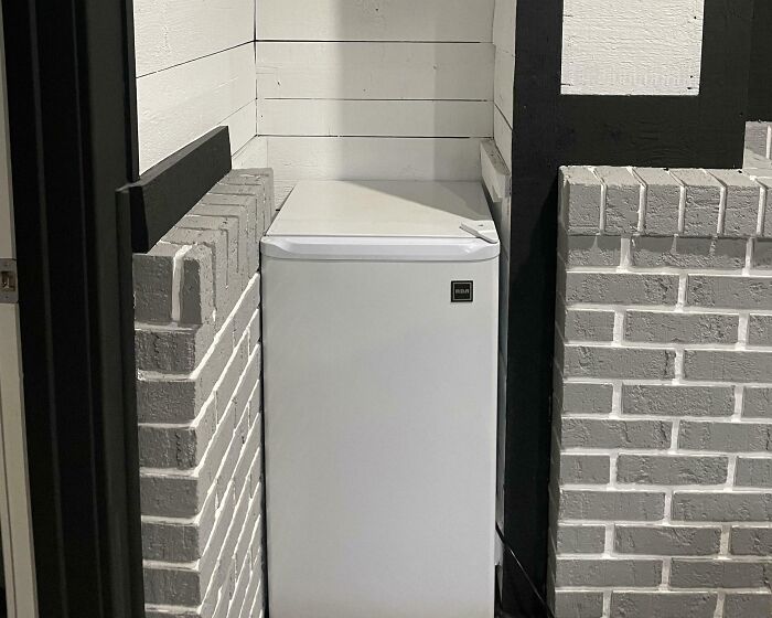 Small white fridge perfectly aligned between two painted brick walls in a narrow corner creating a visually satisfying fit.