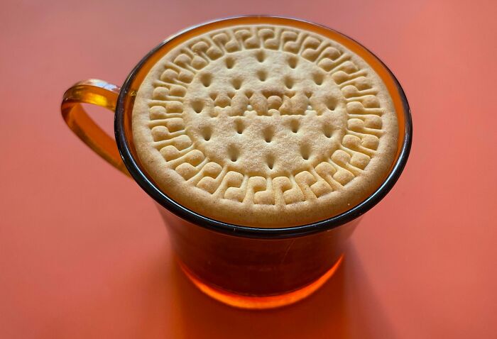 Perfectly aligned biscuit fitting exactly on top of a transparent glass cup, illustrating flawless alignment and symmetry.