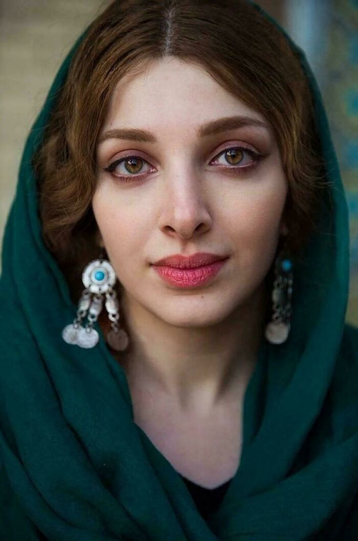 Portrait of a woman wearing traditional earrings and a green headscarf, capturing human beauty and diversity in a close-up view.