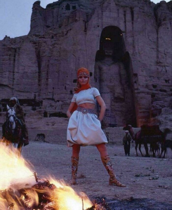 Woman standing confidently near a fire in front of ancient rock carvings, capturing beauty and strength in a portrait.