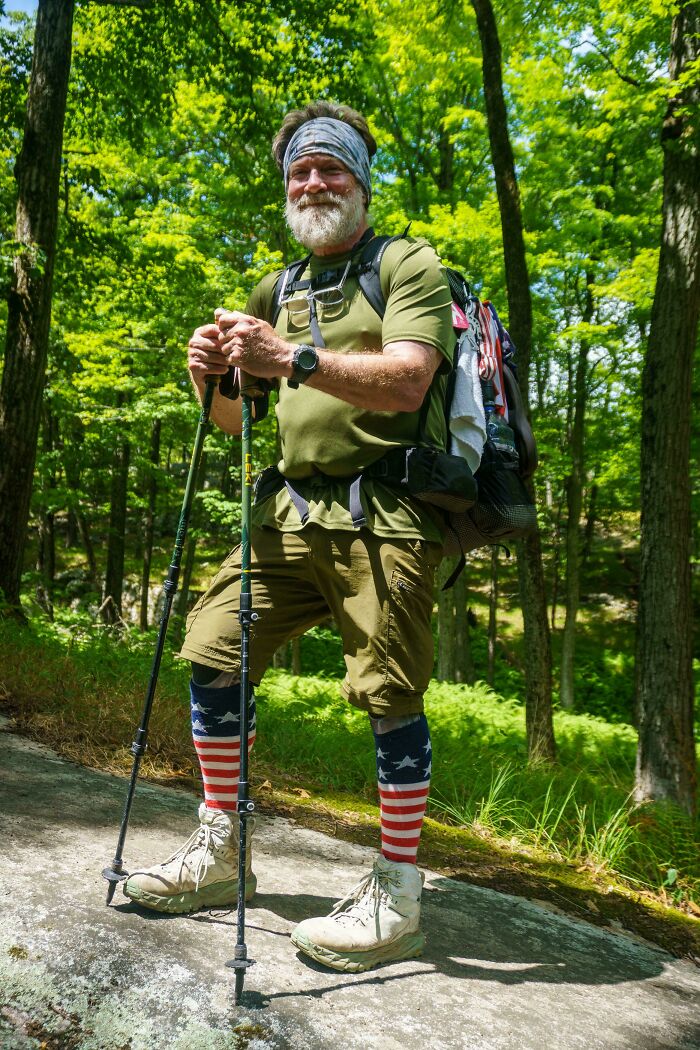 Older hiker with beard and backpack standing in forest, showcasing strength and diversity in outdoor portrait photography.