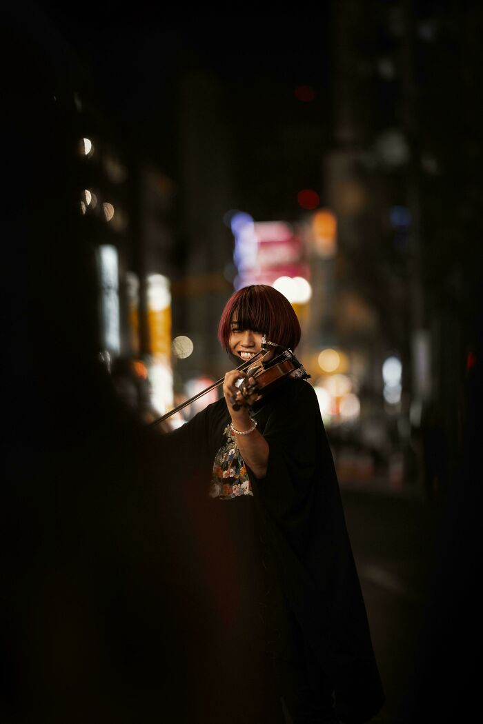 Young violinist smiling while performing at night, capturing the beauty and strength of diverse humans in urban setting