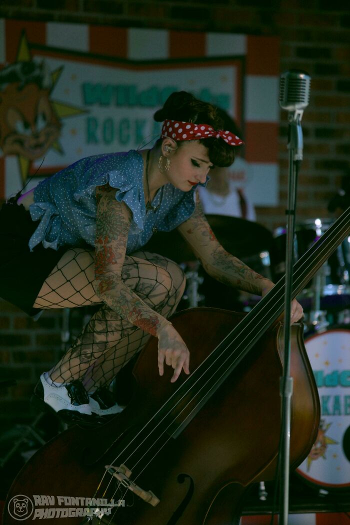 Young tattooed woman with a retro style playing double bass, showcasing strength and diversity in a live music setting.