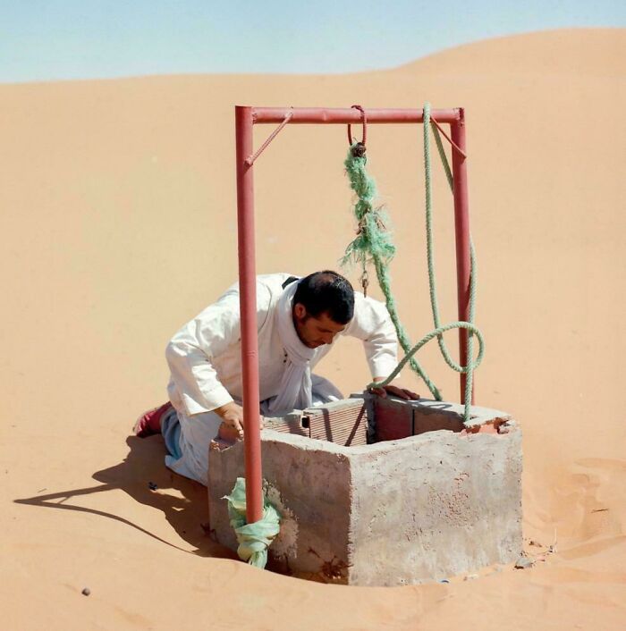 Man drawing water from well in desert, capturing the strength and diversity of humans often overlooked in portraits