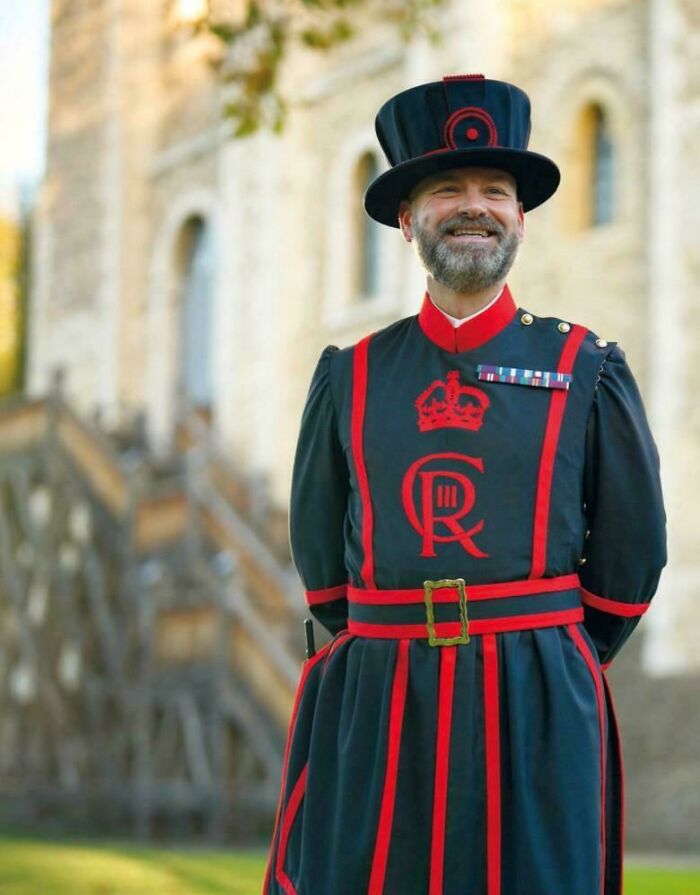 Beefeater in traditional uniform smiling outdoors, a portrait capturing the strength and diversity of humans often overlooked.