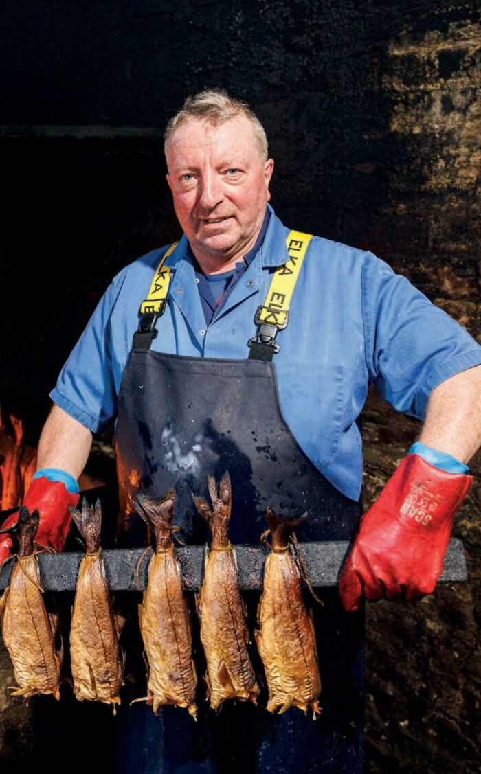 Portrait of a fisherman wearing protective gloves and apron, holding a rack of smoked fish, showcasing human strength and diversity.