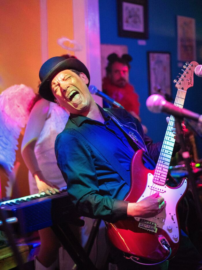 Man playing electric guitar passionately during a lively performance, showcasing the beauty and strength of humans.