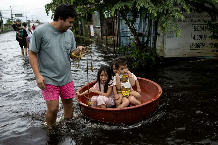 Man pulls three children in a round boat through flooded street, capturing human strength and diversity in challenging conditions.