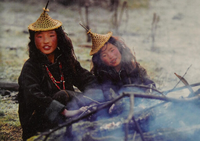 Two children wearing woven hats sit by a campfire, capturing the beauty, strength, and diversity of humans outdoors.