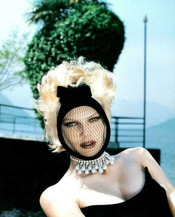 Portrait of a woman with blonde hair wearing a black netted headpiece and pearl necklace, showcasing beauty and diversity in humans.