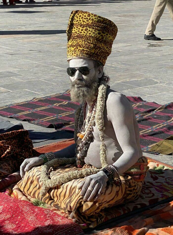 A portrait of a bearded man with body paint, wearing sunglasses and patterned headwear, showcasing human diversity and strength.