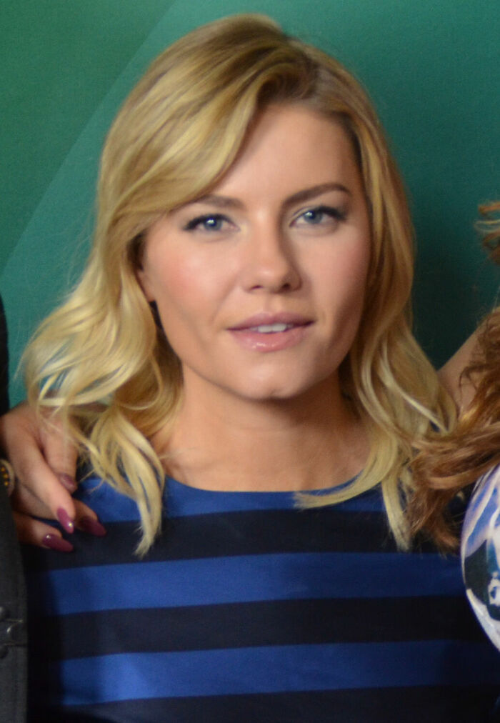Elisha Cuthbert with blonde hair and blue eyes wearing a blue striped shirt against a green background