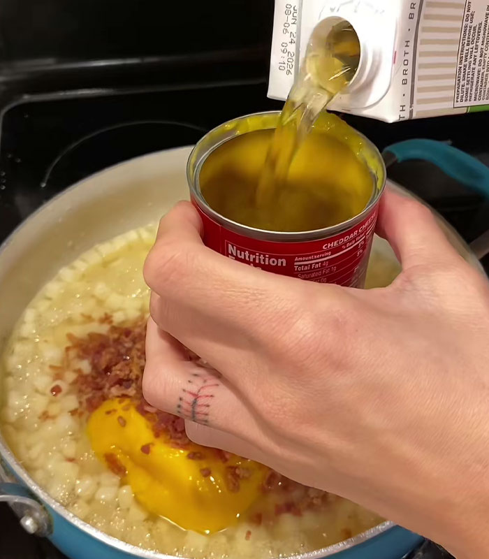 Hand pouring broth into a can of cheddar cheese soup over a pot with cheese and bacon in a wild American food creation. Hand pouring broth into a can of cheddar cheese soup over a pot with cheese and bacon in a wild American food creation.