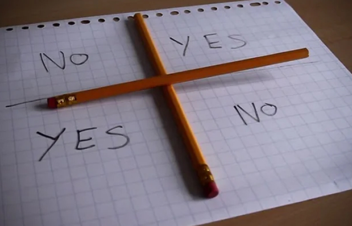 Spirit board setup with pencils on graph paper showing yes and no options for playing scary games with friends IRL.