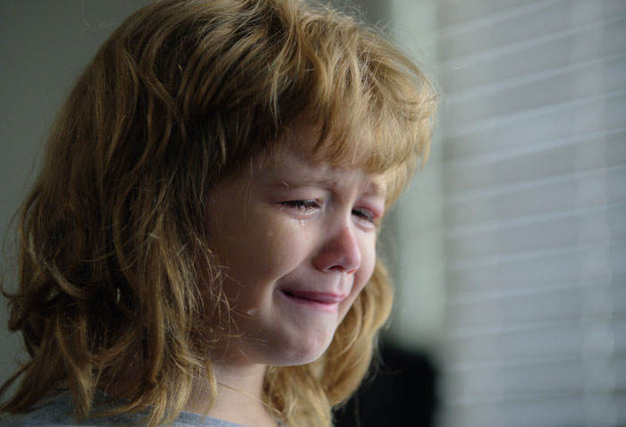 Close-up of a young child crying with visible tears, capturing a raw moment often linked to instant karma situations.