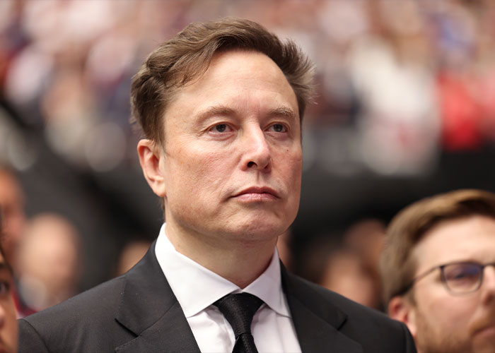 Elon Musk in a dark suit and tie at a public event, photo related to Joyce Carol Oates&rsquo; critical comments.