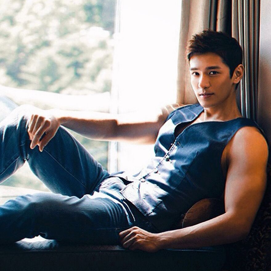 Asian man in sleeveless shirt and jeans relaxing by a window challenging Asian stereotypes in the modern world.