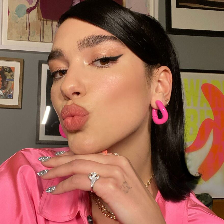 Young woman with pink earrings and glossy lips forming a kiss gesture, illustrating different types of kisses in culture.