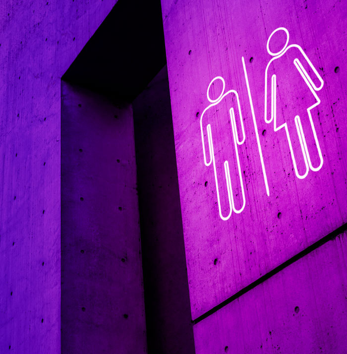Neon restroom signs for men and women on a purple concrete wall, illustrating girl code rules concept.