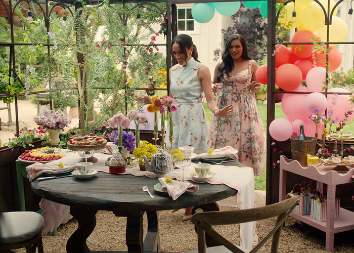 Meghan Markle in a floral dress at a festive garden party, creating a stylish Harper&rsquo;s Bazaar moment.