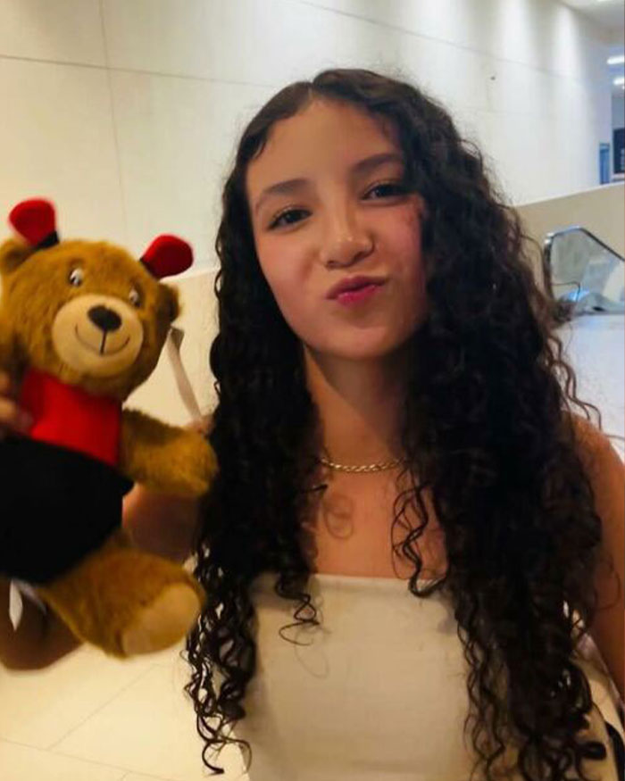 Young woman with curly hair holding a teddy bear, representing women who had a BBL and faced tragic consequences.