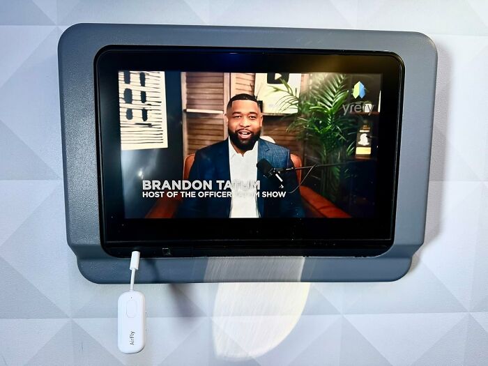 Small screen device mounted on a wall playing a podcast video with tech accessories nearby Black Friday tech deals.