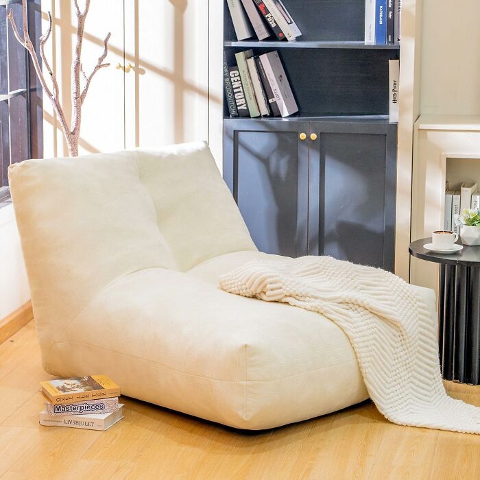 Cozy lounge chair with soft cream fabric and a knitted throw blanket in a warm, inviting living space.