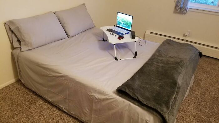 Bed with gray sheets and blanket, laptop on a portable desk, illustrating Black Friday deals for procrastinators.