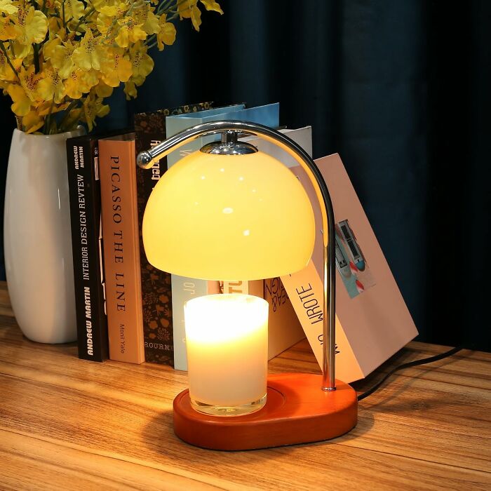 Modern aesthetic desk lamp with candle on wooden table beside books and yellow flowers in white vase