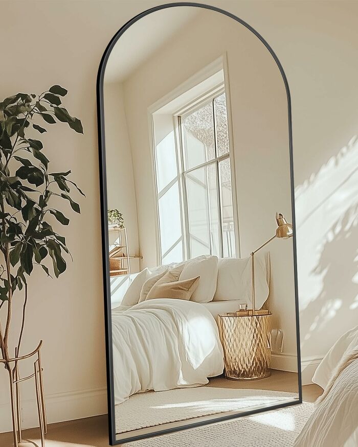 Arched floor mirror reflecting a bright bedroom with a bed and golden side table, highlighting 11.11 deals for lucky shoppers.