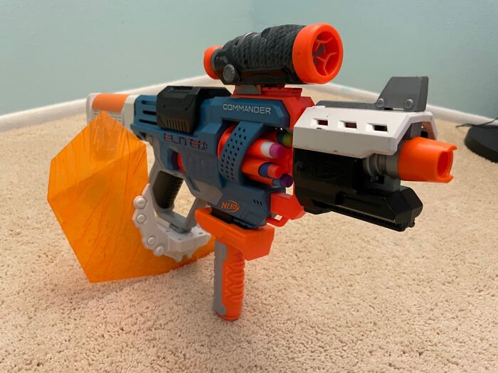 Nerf gun toy with scope and orange darts on carpet, featured in Black Friday week deals on kids toys for Christmas.