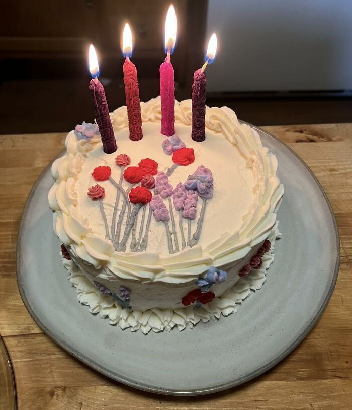 White frosted cake with red and purple floral designs and four lit candles, perfect for Black Friday deals celebration.
