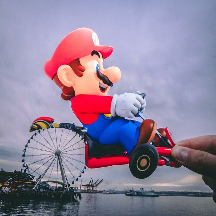 Paper cutout of a Mario character creatively interacting with real-life Ferris wheel and waterfront background.