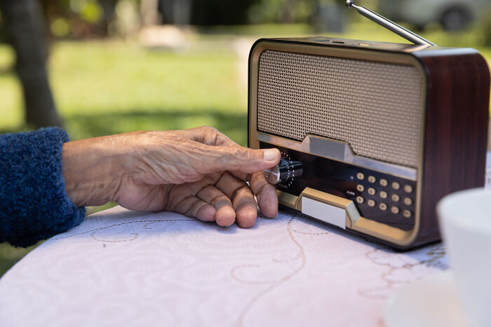An elderly man's hand adjusting the k**b on a vintage radio, capturing lovable clueless dads moments.