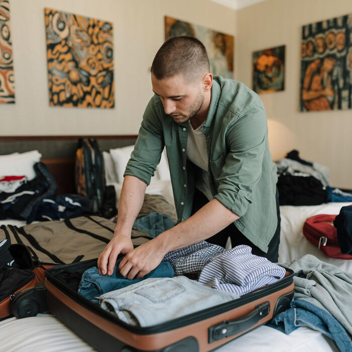 Young man packing clothes into suitcase in a hotel room, illustrating people who disappeared to start new lives experiences.