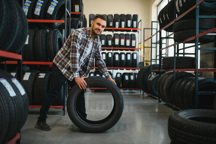 Man in plaid shirt holding tire in a tire shop, illustrating insider experiences shared by nepo babies.