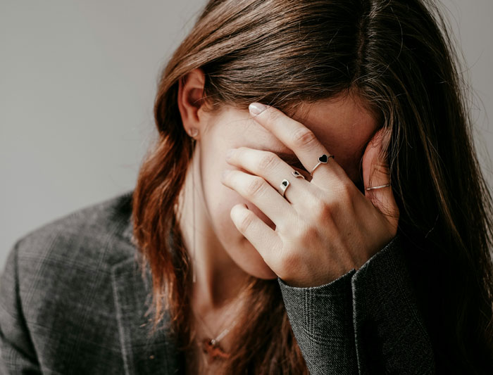 Woman shocked and confused, covering her face with hand, refusing to pay for borrowed dress altered without permission.
